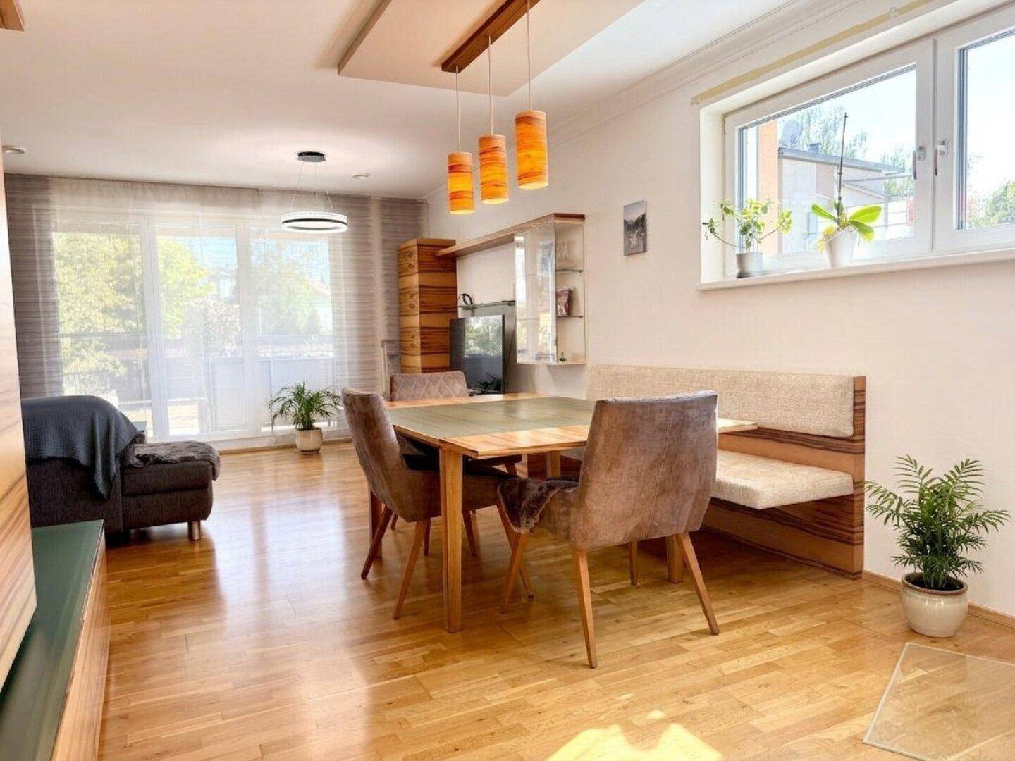 Heller Wohn-Essbereich mit Holzboden, großem Esstisch und Zugang zum Balkon.