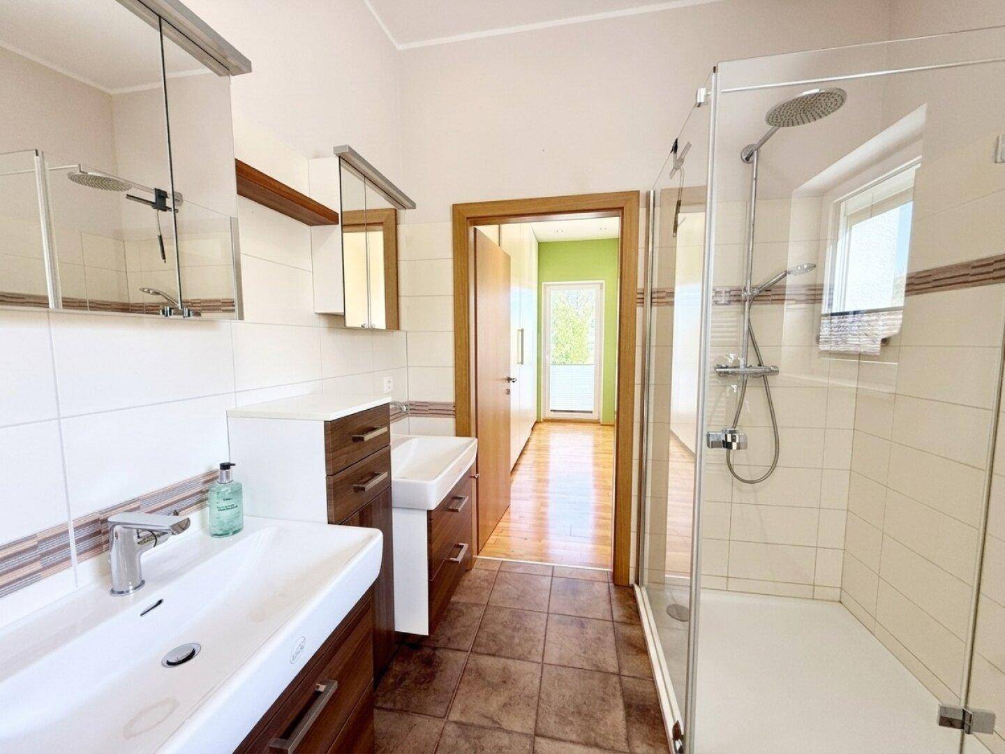 Geräumiges Badezimmer mit Doppelwaschbecken, großer Duschkabine und Fenster.