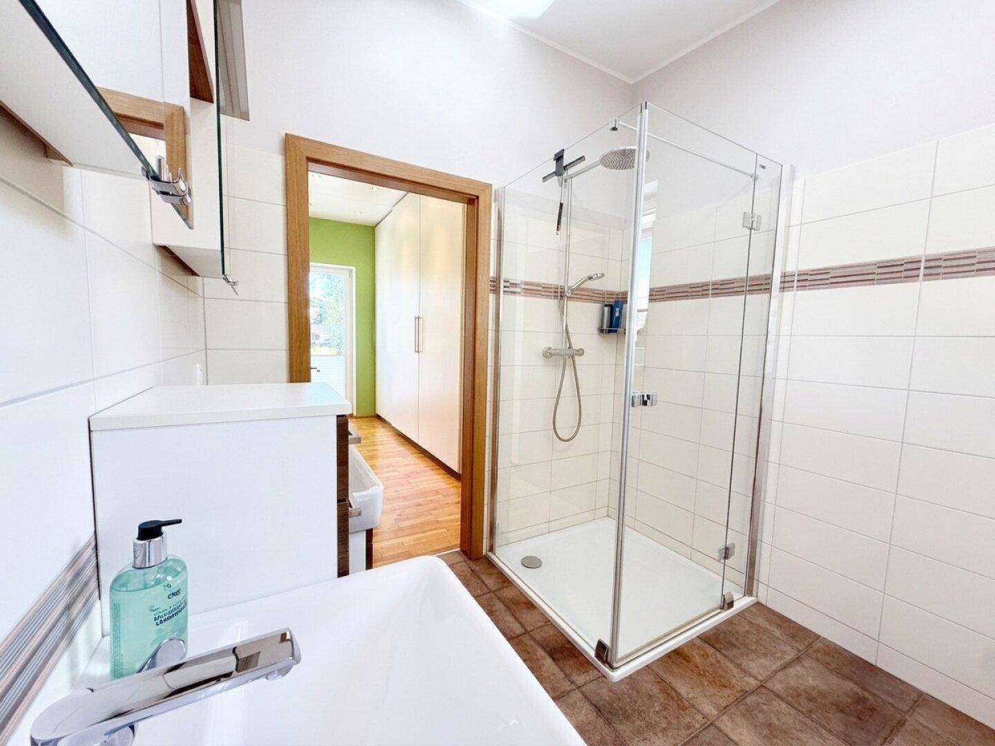 Modernes Badezimmer mit Duschkabine, Einzelwaschbecken und hellen Fliesen.