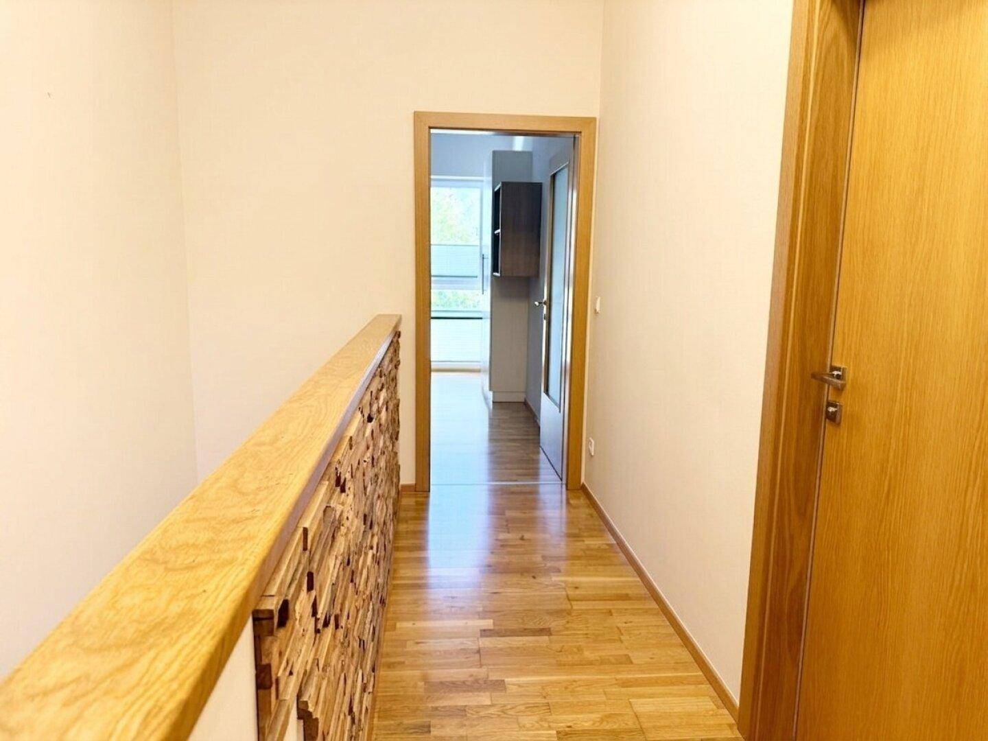 Heller Flur im Obergeschoss mit Holzboden und Holzgeländer, der zu den Zimmern führt.