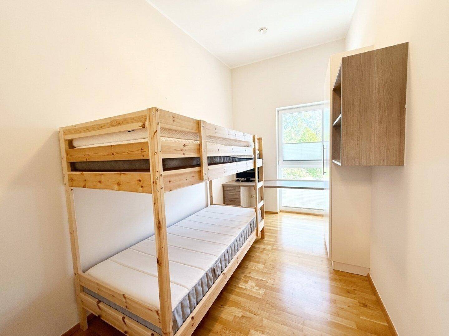 Kinderzimmer mit Etagenbett, Holzboden und Fenster, das viel Tageslicht hereinlässt.
