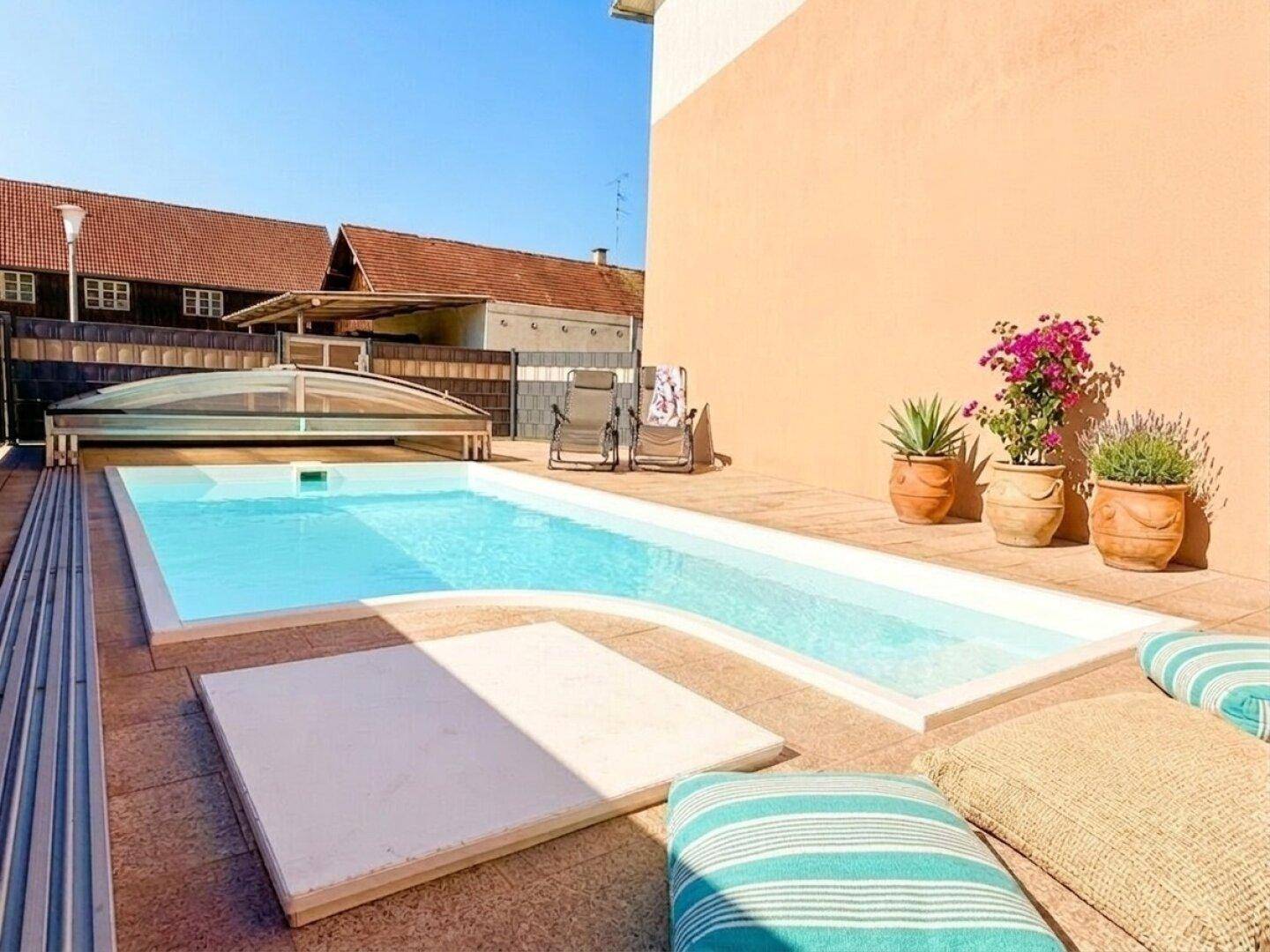 Sonniger Poolbereich mit Liegestühlen und Pflanzen, perfekt zum Entspannen an warmen Tagen.