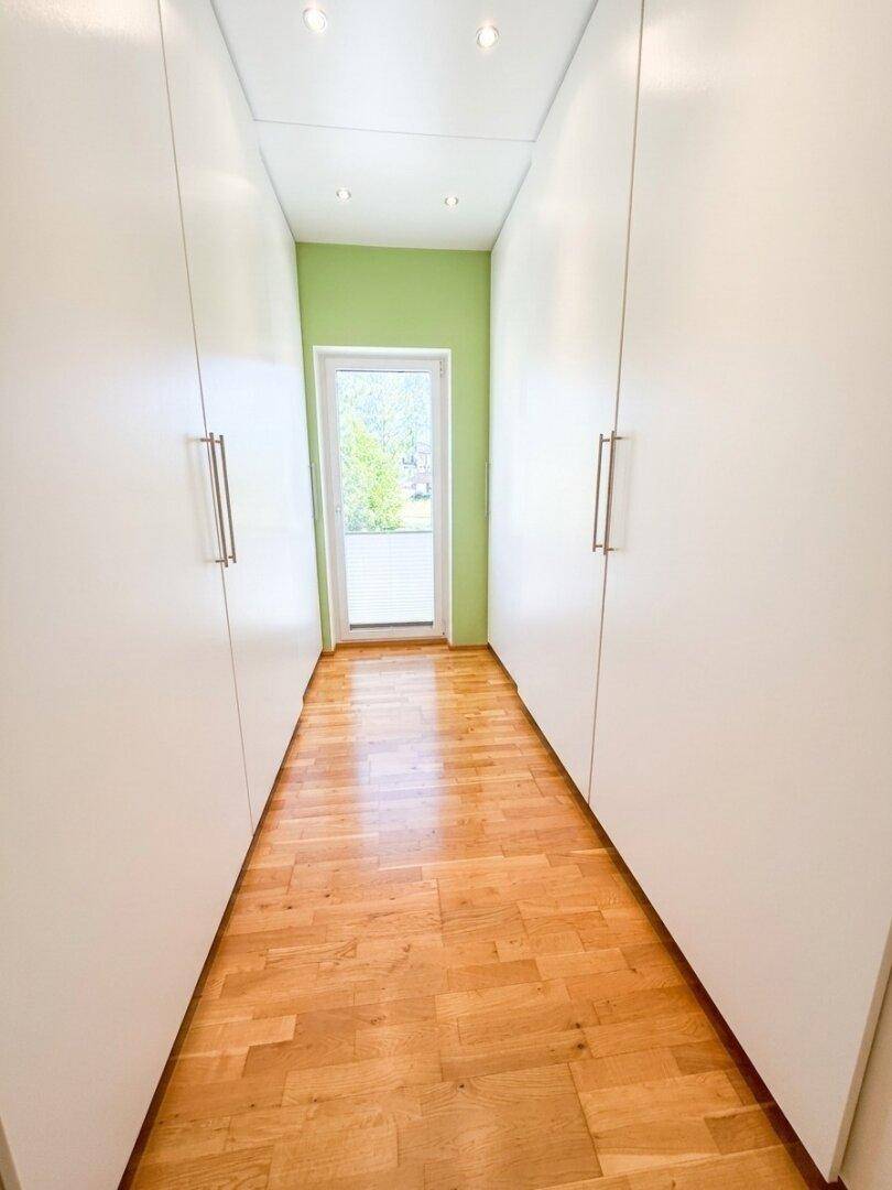 Heller Flur mit Einbauschränken und Holzboden, der zu einem weiteren Raum führt.