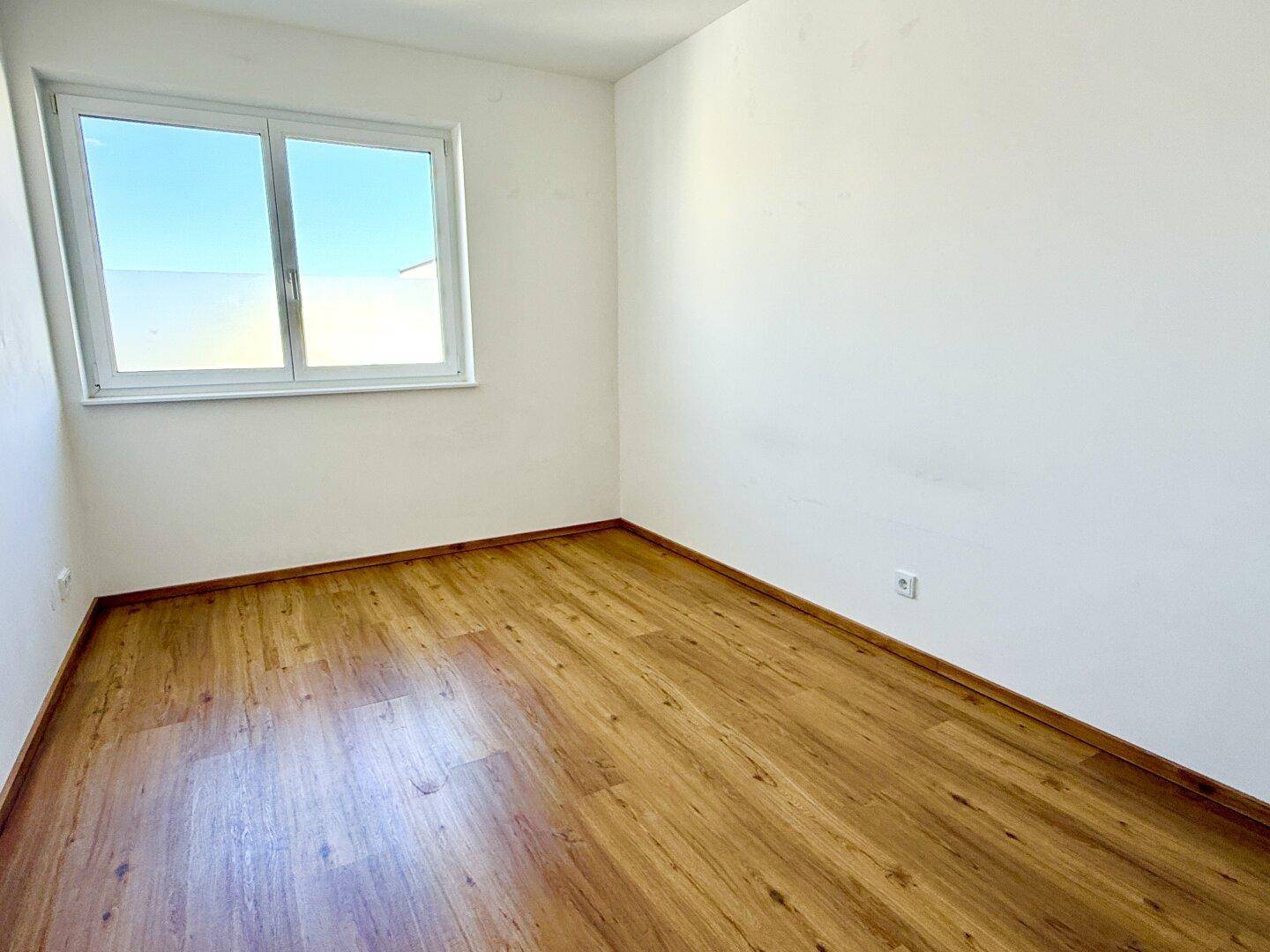 Helles, leeres Schlafzimmer mit Laminatboden und großem Fenster, bereit zur Einrichtung.