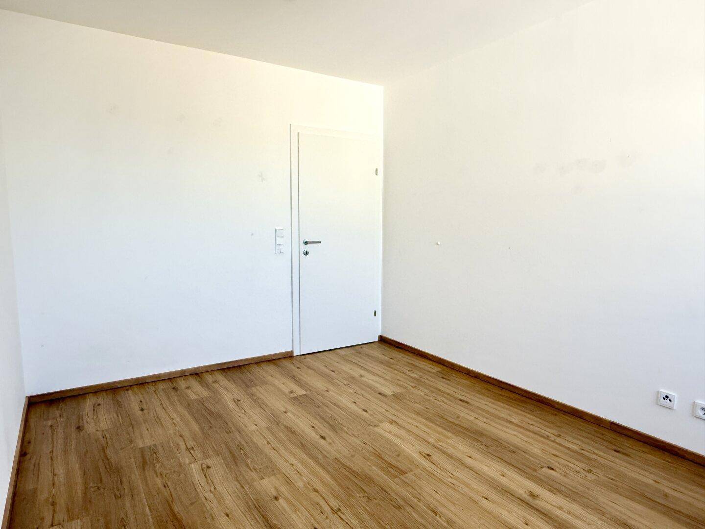 Leeres Schlafzimmer mit Laminatboden und weiß gestrichenen Wänden, ideal für individuelle Gestaltung.