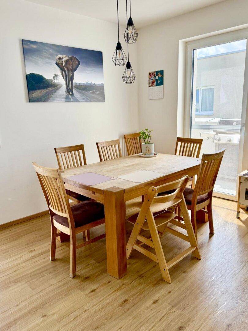 Heller Essbereich mit großem Holztisch, passenden Stühlen und Zugang zum Balkon.