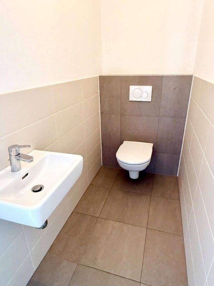 Modernes Gäste-WC mit wandhängender Toilette, kleinem Waschbecken und Fliesen.