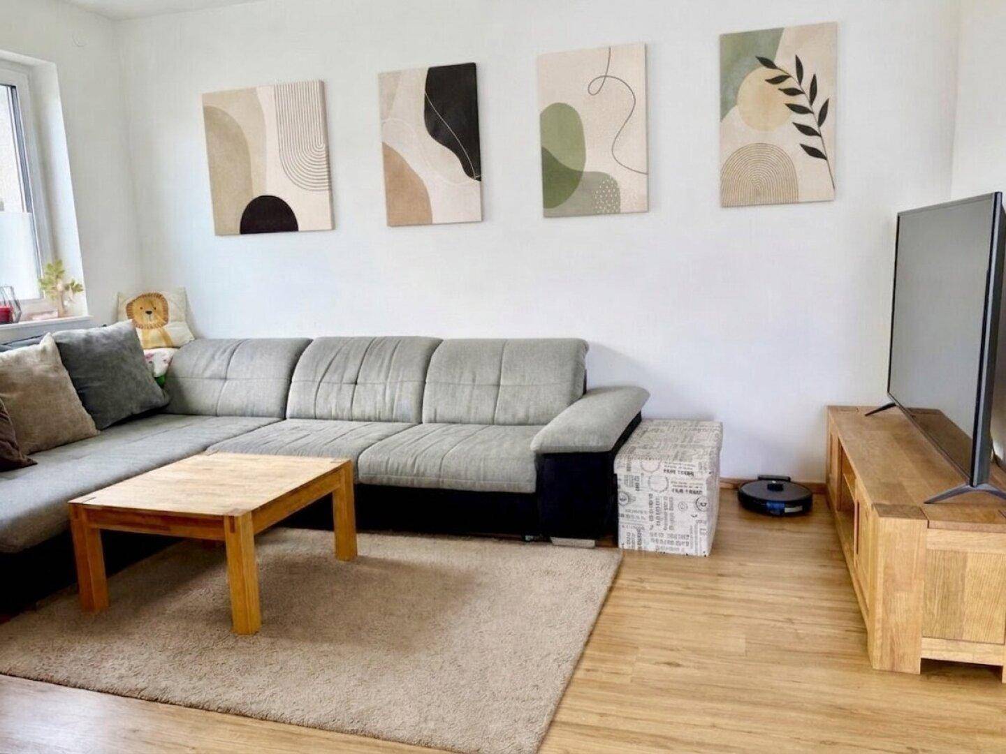 Gemütliches Wohnzimmer mit großem Ecksofa, Holzboden und moderner Wanddekoration.
