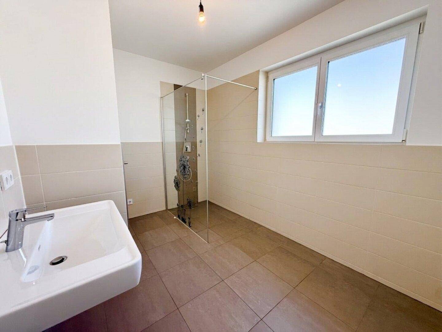 Helles Badezimmer mit ebenerdiger Dusche, Waschbecken und Fenster für Tageslicht.
