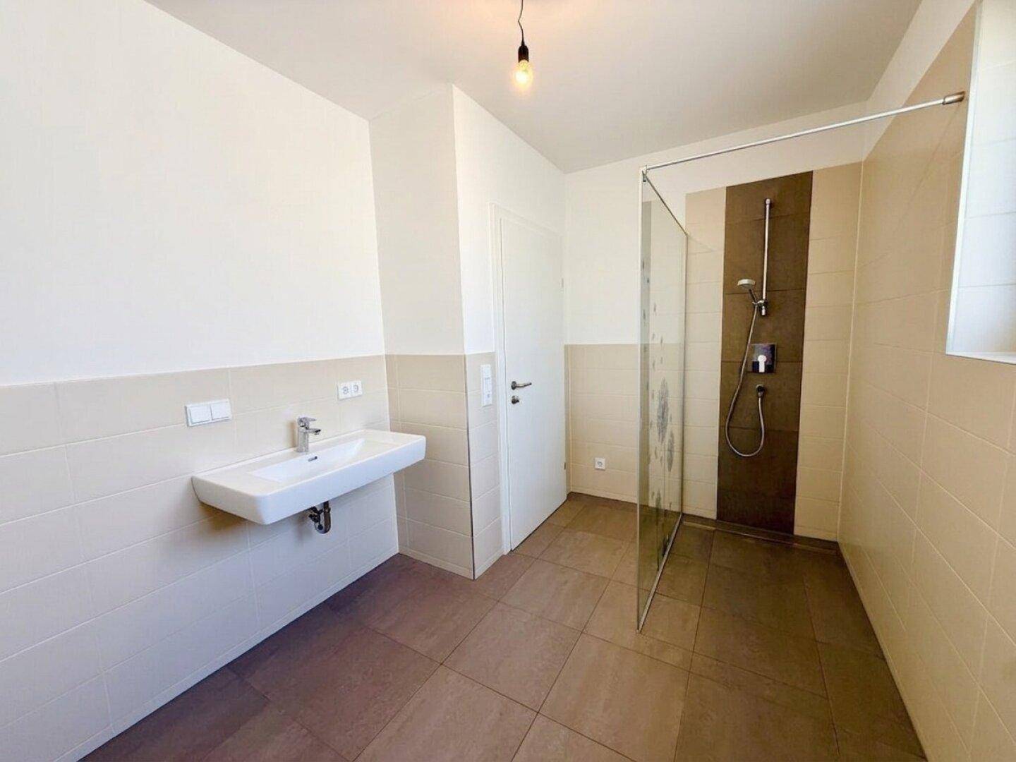 Modernes Badezimmer mit großer Duschkabine, Waschbecken und hellen Fliesen.