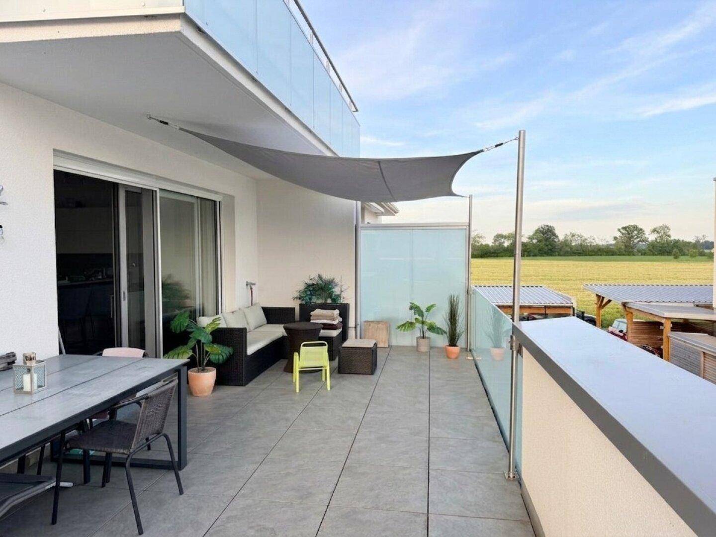 Große, möblierte Terrasse mit Sonnensegel und Blick ins Grüne, perfekt für Mahlzeiten im Freien.
