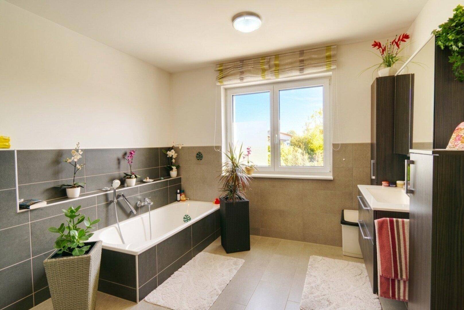 Geräumiges Badezimmer mit Badewanne, Doppelwaschbecken und großem Fenster für Tageslicht.