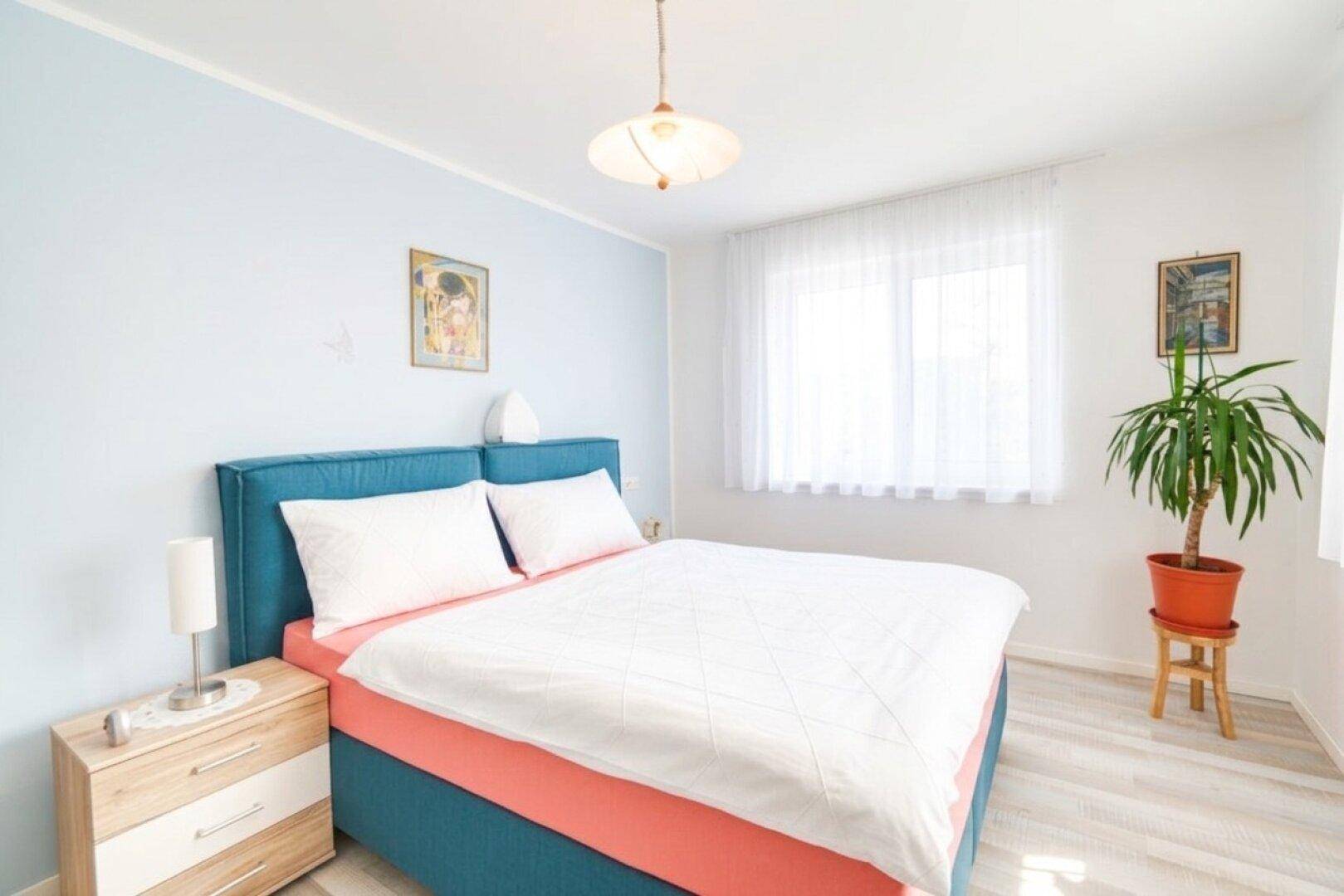 Helles Schlafzimmer mit modernem Bett, Nachttisch und großem Fenster für viel Tageslicht.