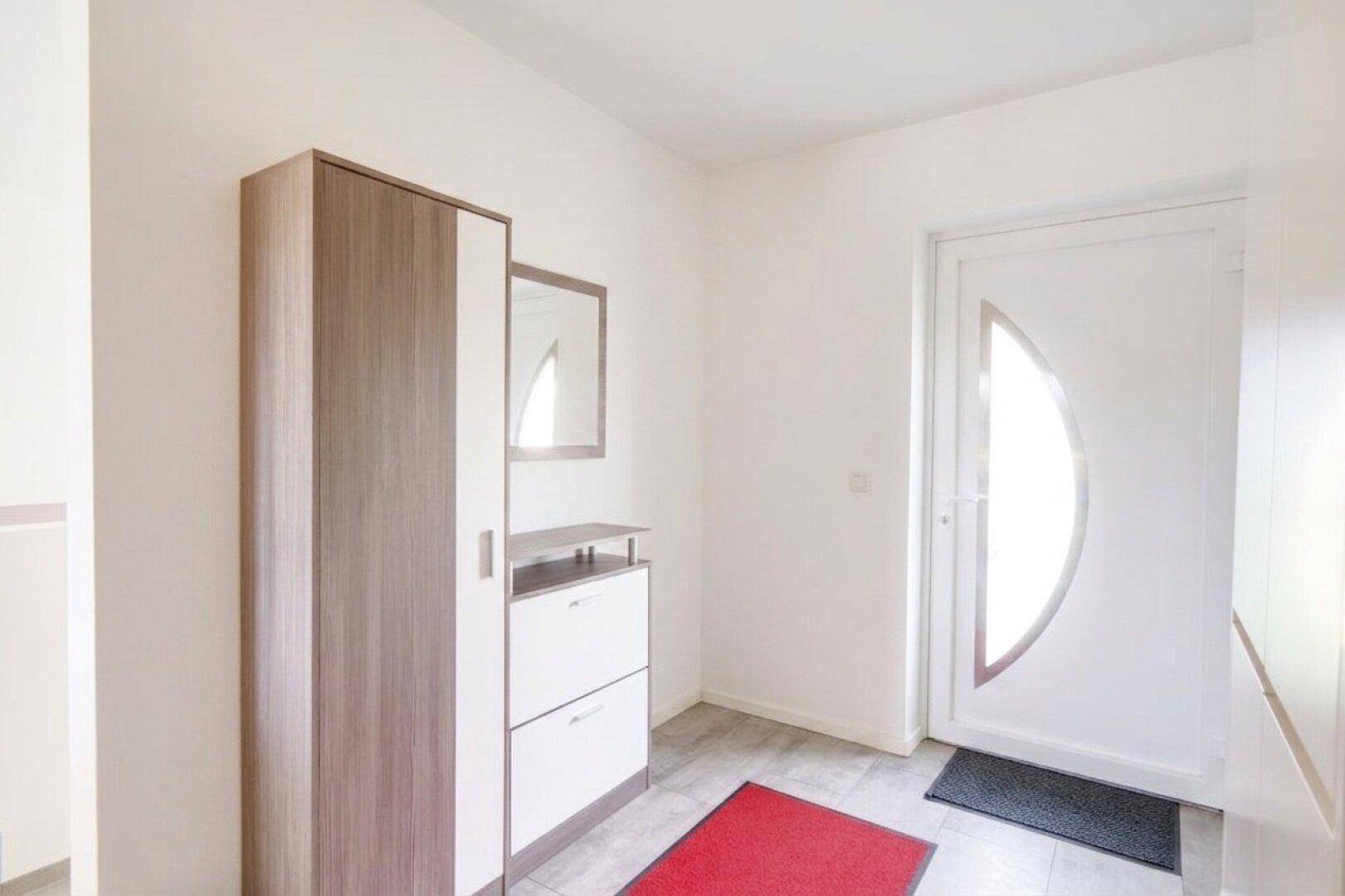 Heller Eingangsbereich mit moderner Garderobe, Schuhschrank und freundlicher Eingangstür.