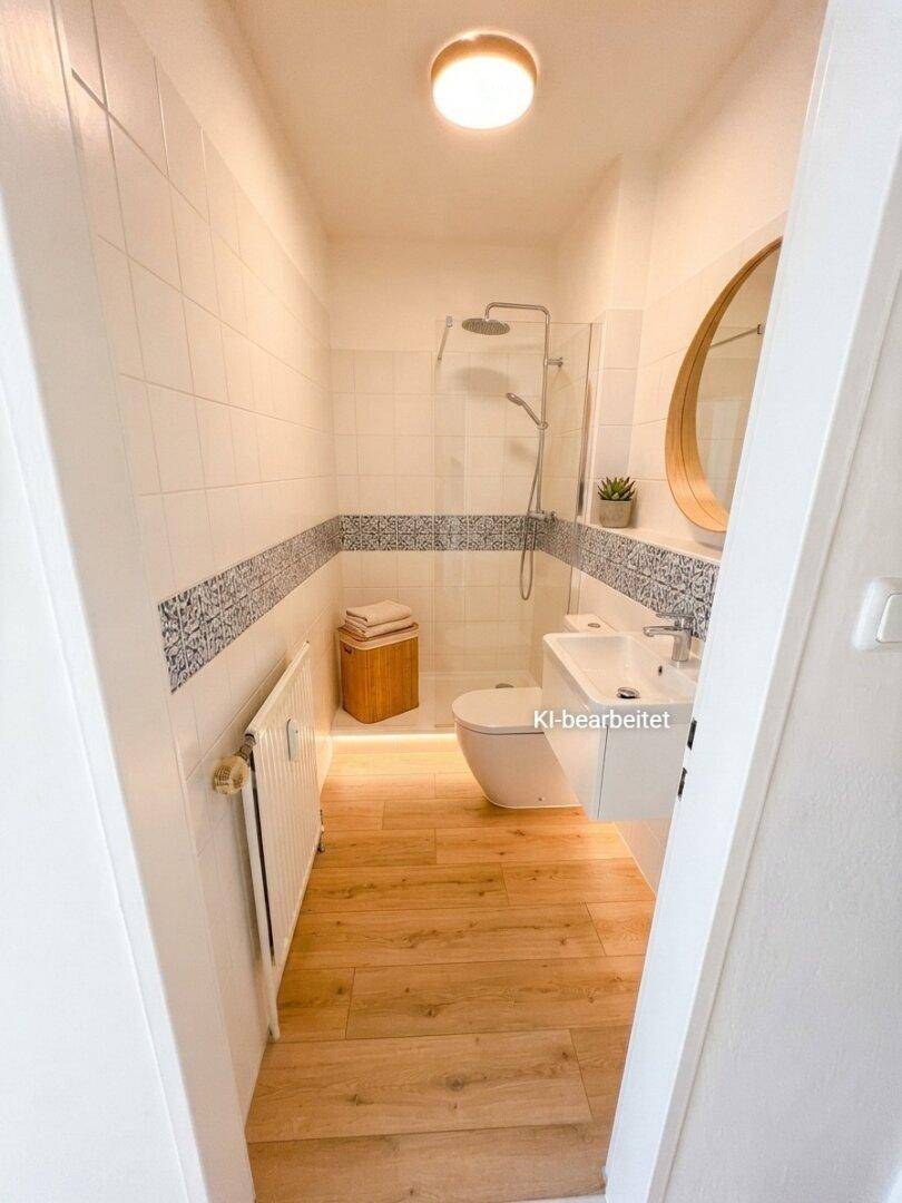 Modernisiertes Badezimmer mit begehbarer Dusche, Wand-WC, Holzoptikboden und dekorativen Fliesen.