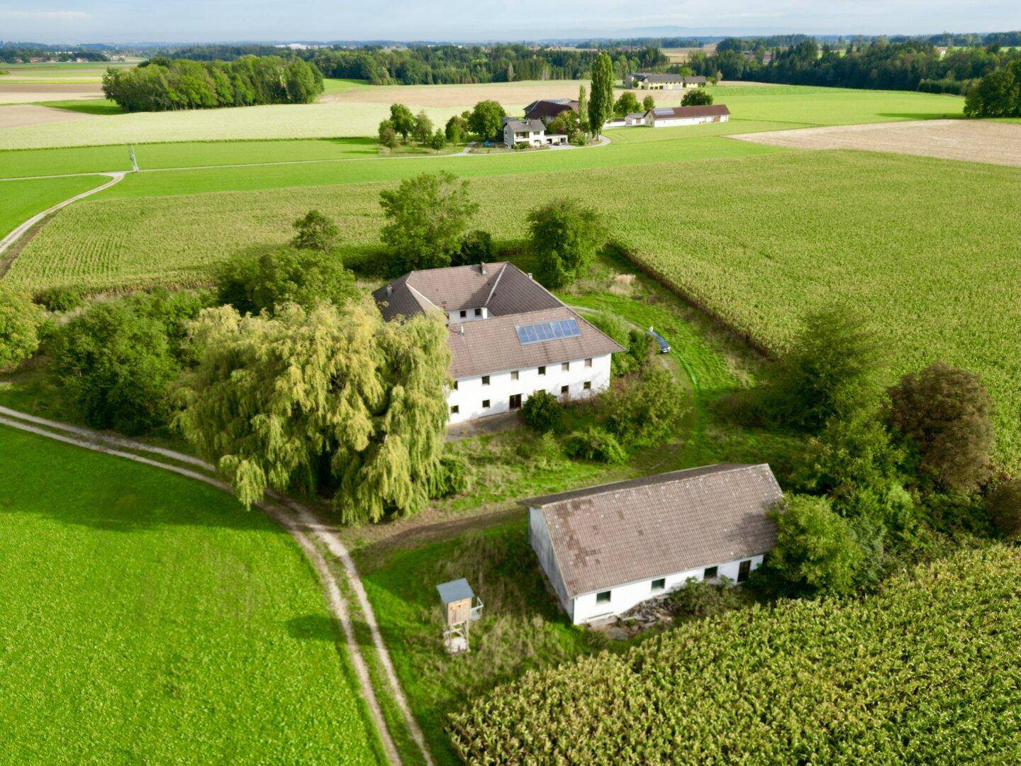 Weitläufige Luftansicht des Anwesens mit Haupthaus und Nebengebäude inmitten landwirtschaftlicher Flächen.