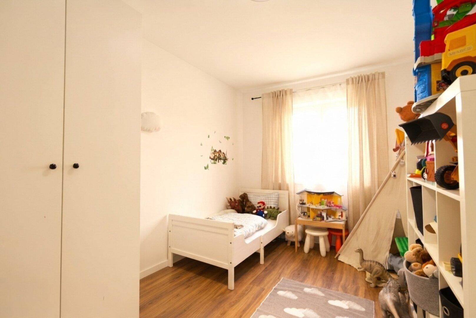 Helles Kinderzimmer mit Holzbett, Spielzeug und Laminatboden.