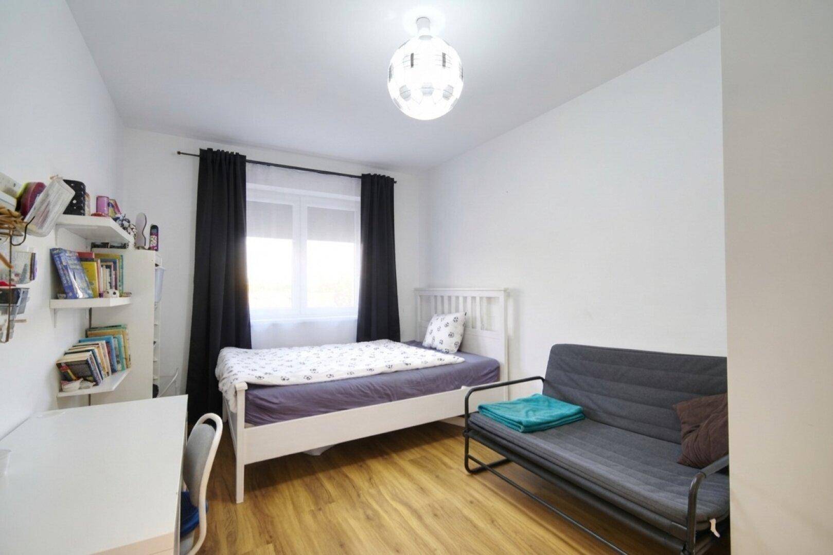 Freundliches Zimmer mit Einzelbett, Schreibtisch und Sofa, ideal als Gäste- oder Arbeitszimmer.