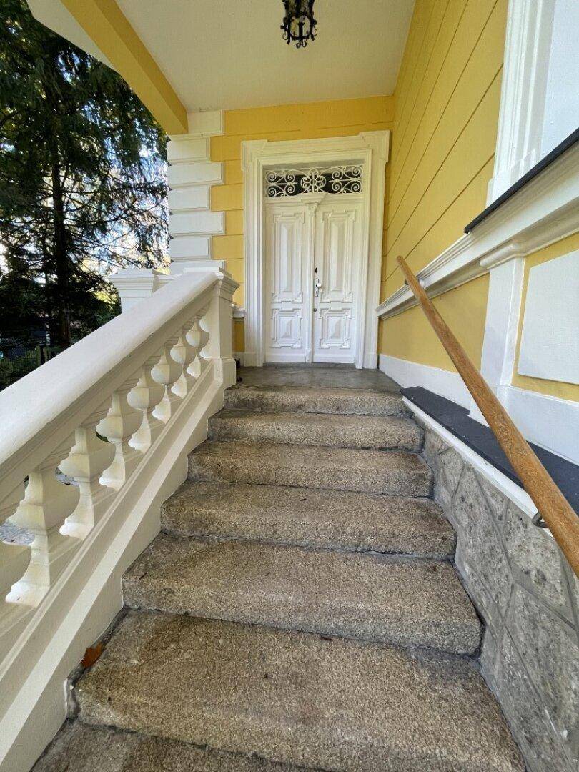 Historischer Eingangsbereich mit Steintreppe, verzierten Geländern und einer eleganten weißen Doppeltür zum Gebäude.