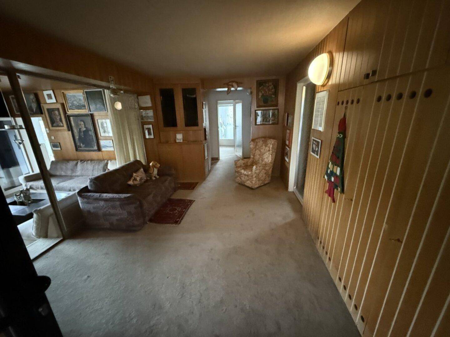 Gemütliches Wohnzimmer mit Holzvertäfelung, Teppichboden und vielen gerahmten Bildern an den Wänden.