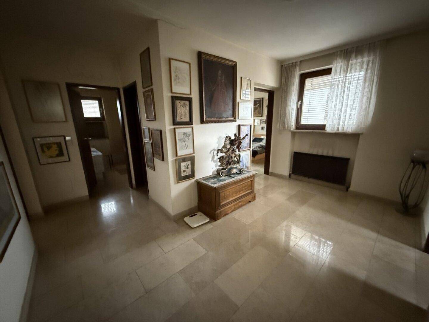 Heller Flur mit Fliesenboden, vielen Bildern an den Wänden und einem dekorativen Holzschrank.