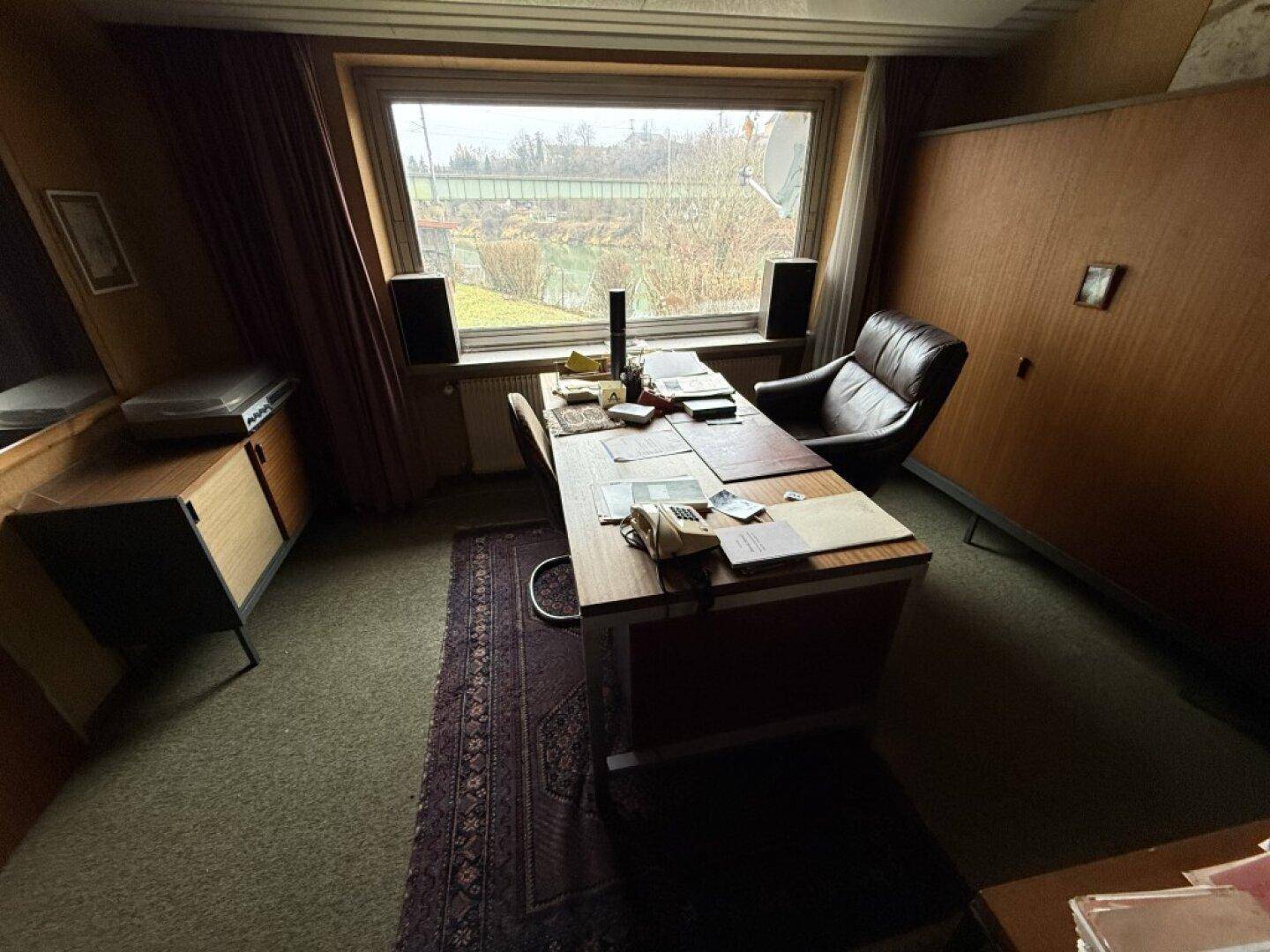 Klassisches Büro mit Schreibtisch, Ledersessel und Blick auf die Umgebung durch ein großes Fenster.