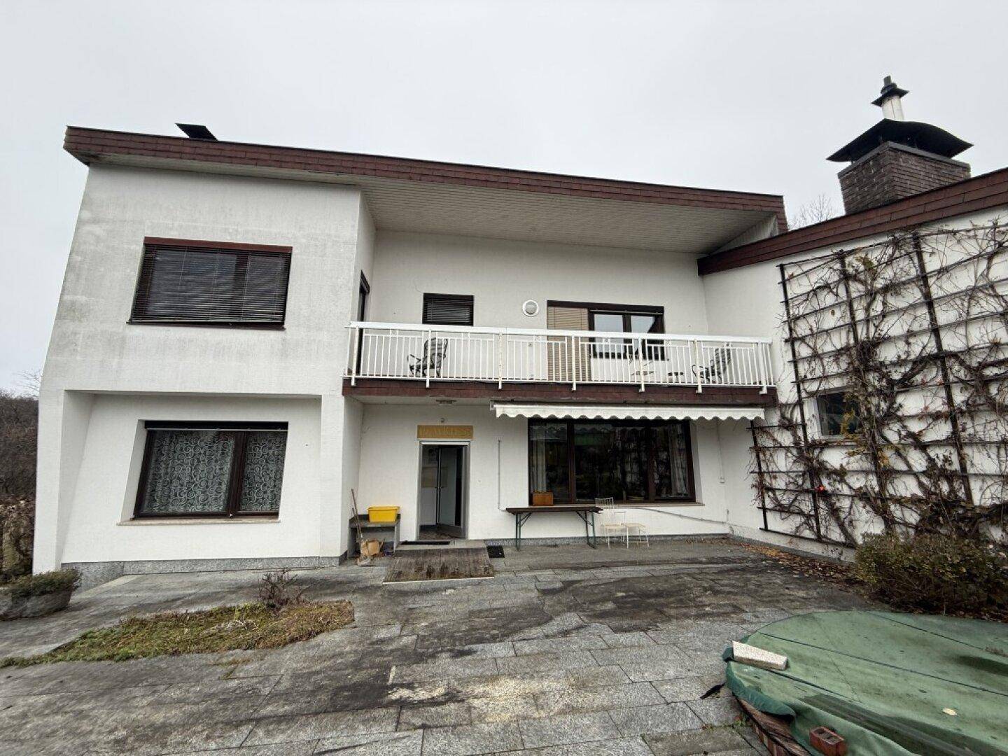 Die Rückseite des Hauses mit einem Balkon im Obergeschoss und einer gepflasterten Terrasse im Erdgeschoss.