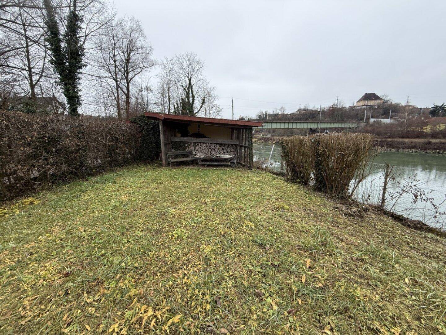 Kleiner Holzunterstand im Gartenbereich am Flussufer, ideal für Lagerung oder als gemütlicher Rückzugsort.