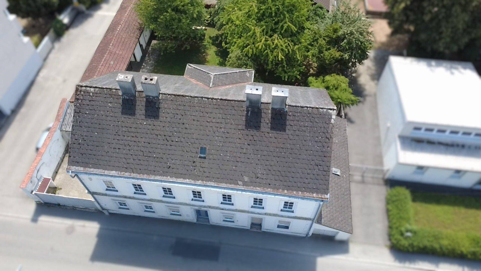Vogelperspektive des Wohnhauses mit Dach und angrenzenden Gebäuden, sowie der Straße.