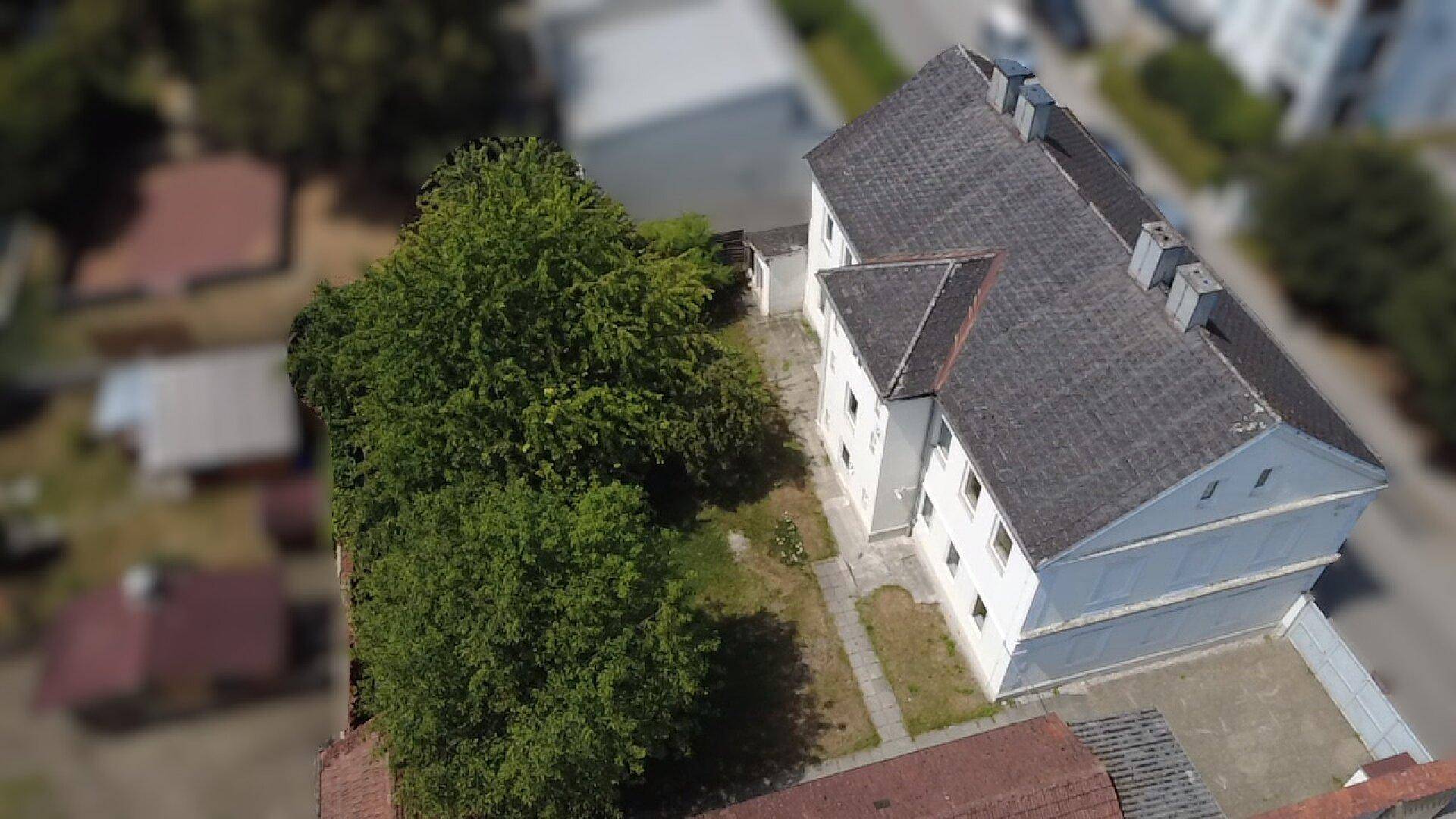 Luftaufnahme des Gebäudes von der Seite mit Bäumen und der Dachstruktur, die das Grundstück umgibt.