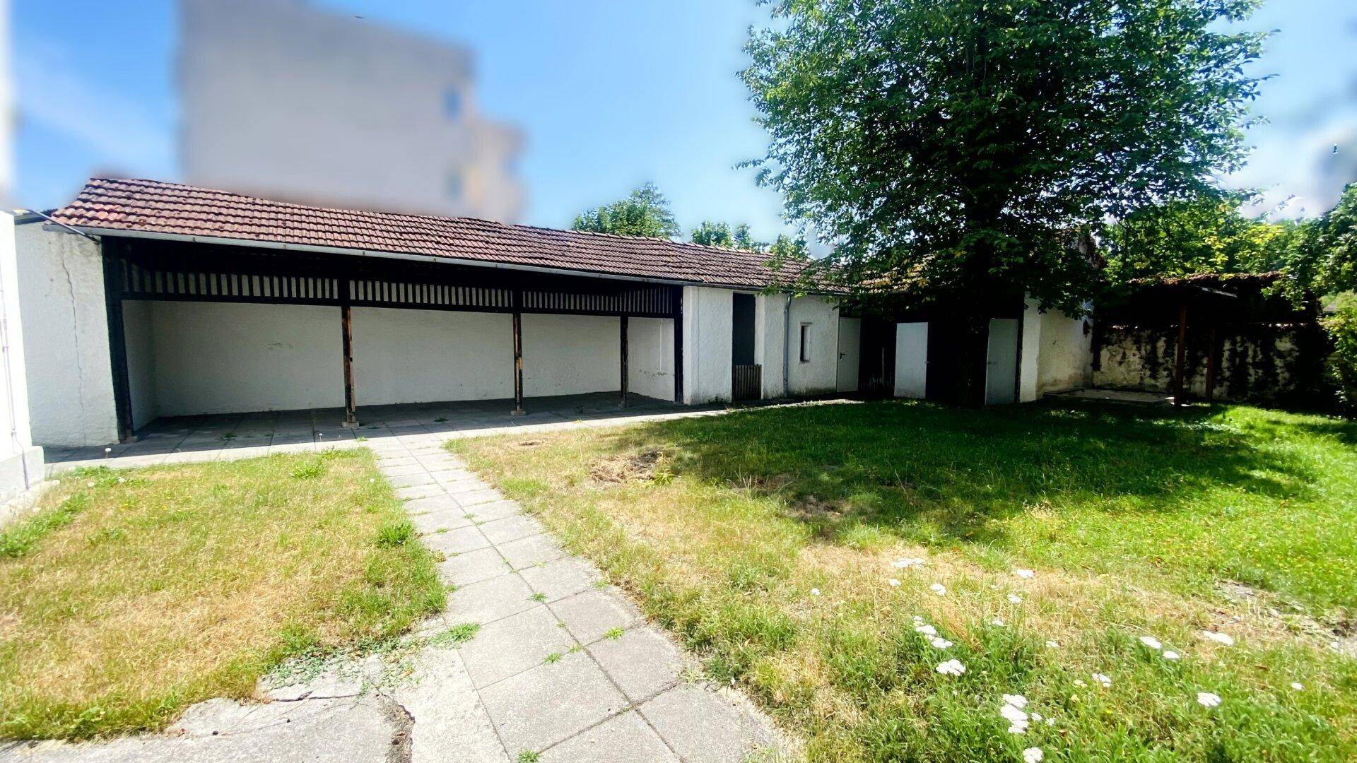 Hinterhof mit Rasenfläche, gepflastertem Weg und einem langen Schuppen oder Carport im Hintergrund.