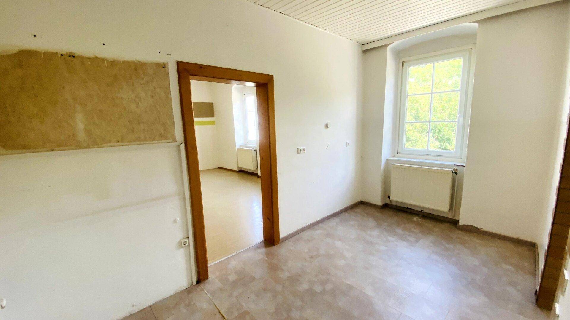 Schlafzimmer mit Holztürrahmen, Fenster und Blick auf die grüne Umgebung, bereit zur Renovierung.