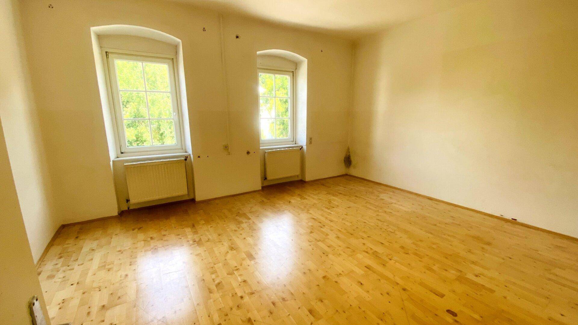 Geräumiges Schlafzimmer mit zwei Fenstern, Parkettboden und viel Tageslicht.