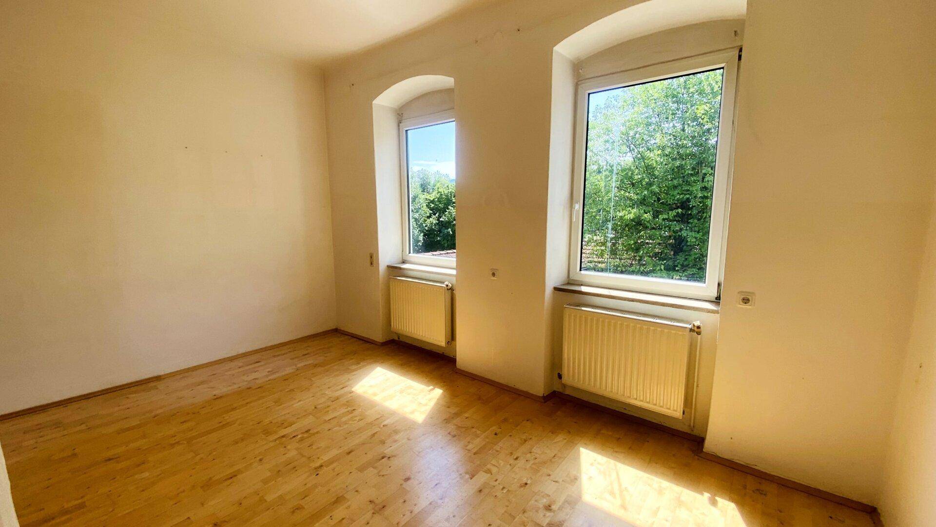 Schlafzimmer mit zwei Fenstern, die viel Licht hereinlassen und einen Blick ins Grüne bieten.
