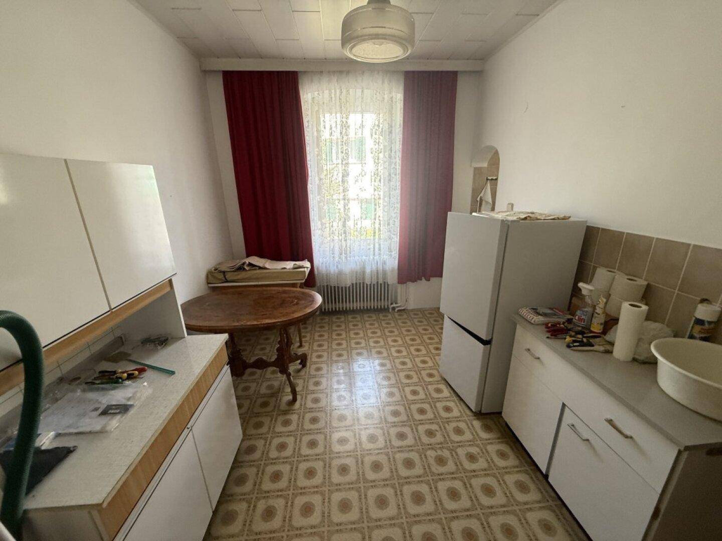 Einfache Küche mit gemustertem Linoleumboden, Kühlschrank und kleinem Esstisch.