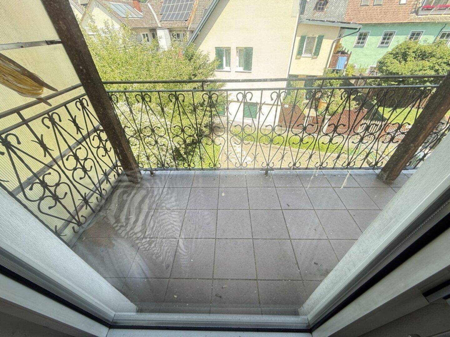 Überdachter Balkon mit schmiedeeisernem Geländer und Blick auf umliegende Gärten und Dächer.
