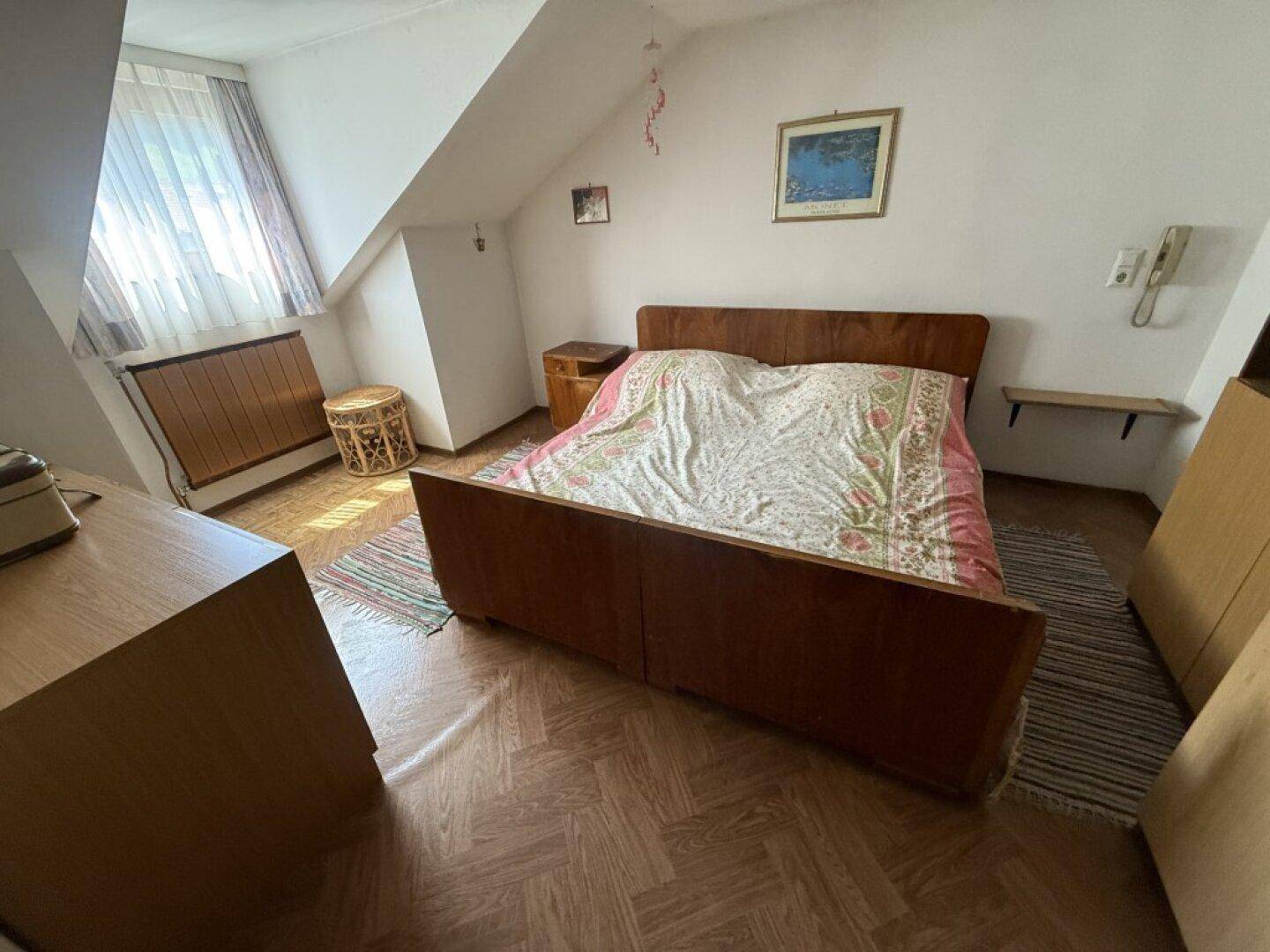 Schlafzimmer im Dachgeschoss mit schrägen Wänden, Holzboden und einem Doppelbett.