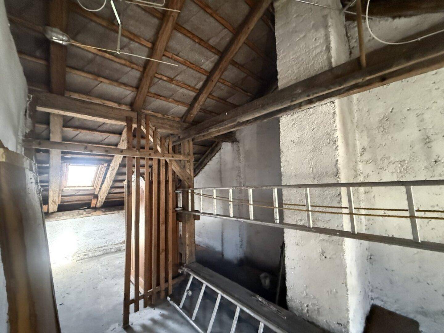 Unausgebauter Dachboden mit sichtbaren Holzbalken und Dachfenster, bietet Ausbaupotenzial.