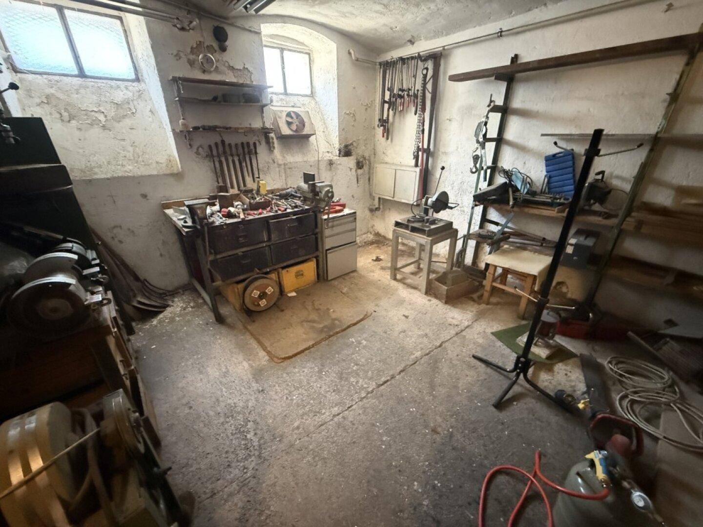Werkstatt im Keller mit Betonboden, Werkbänken und verschiedenen Werkzeugen.