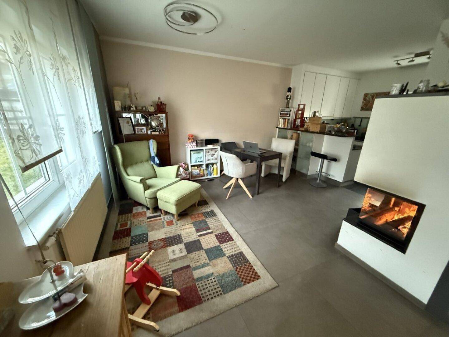 Gemütlicher Wohnbereich mit Kamin, Sessel und offenem Übergang zum Essbereich.