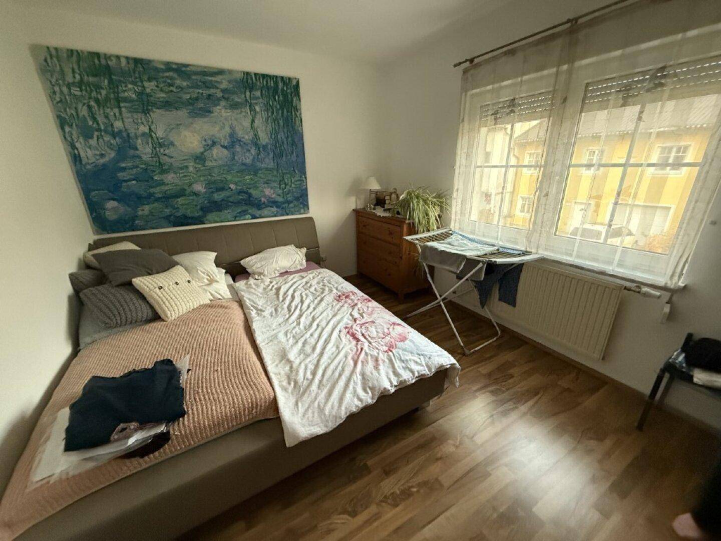 Helles Schlafzimmer mit Doppelbett, Kommode und großem Fenster mit Blick nach draußen.