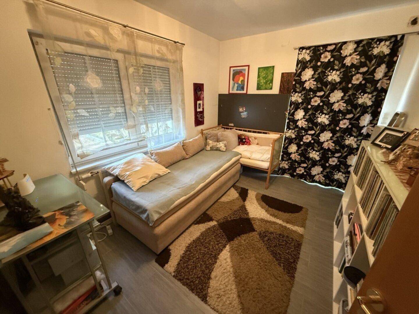 Gemütliches Schlafzimmer mit Tagesbett, Schreibtisch und Fenster mit Rollläden.