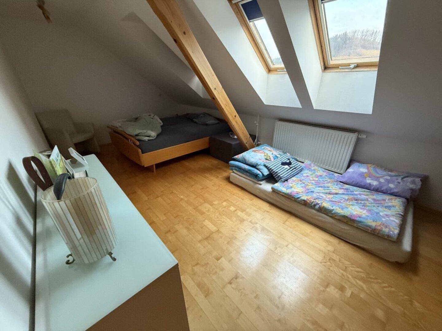Helles Dachzimmer mit Holzbalken, Dachschrägen und zwei Dachfenstern für viel Licht.