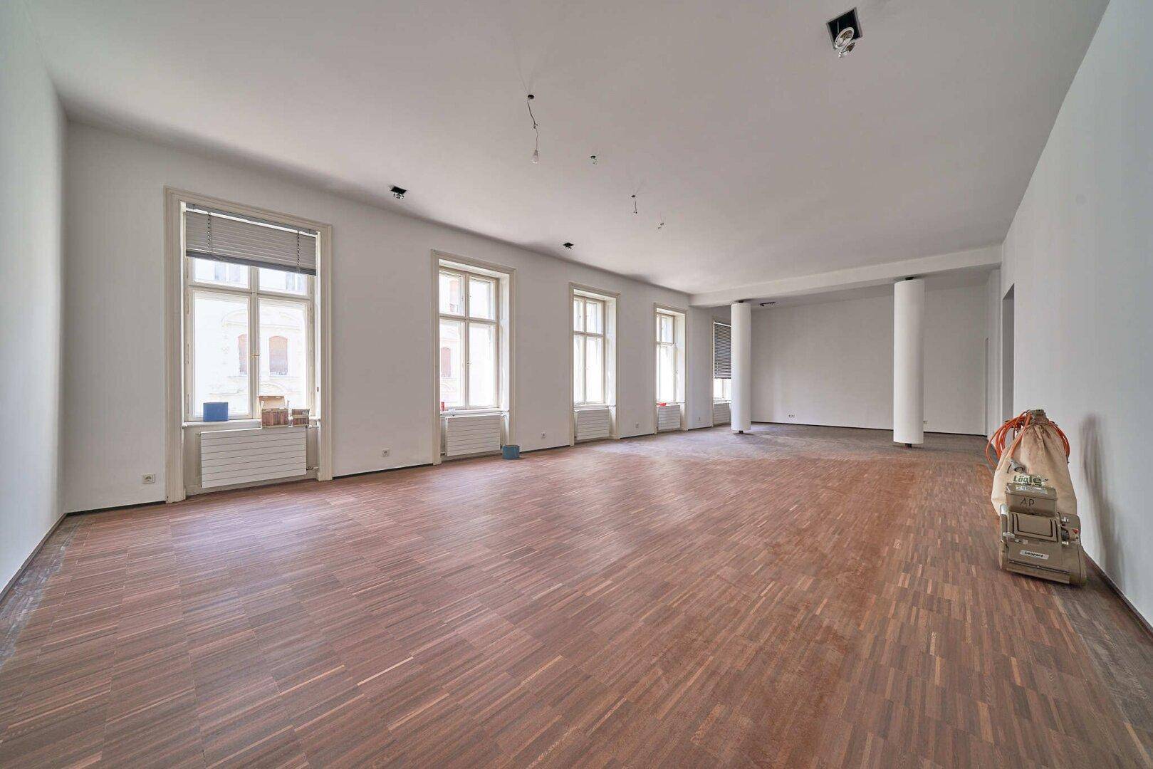 Geräumiger, heller Innenraum mit hohen Fenstern und Holzboden, bereit für die Gestaltung.