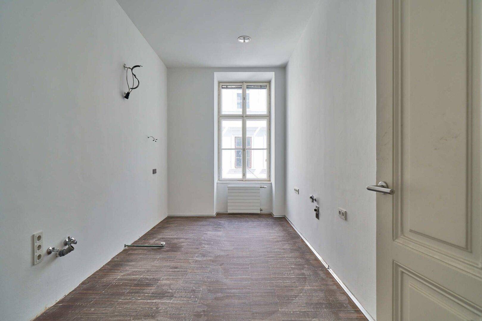 Schmaler Raum mit Fenster und Anschlüssen für eine Küche, bereit zur Installation.