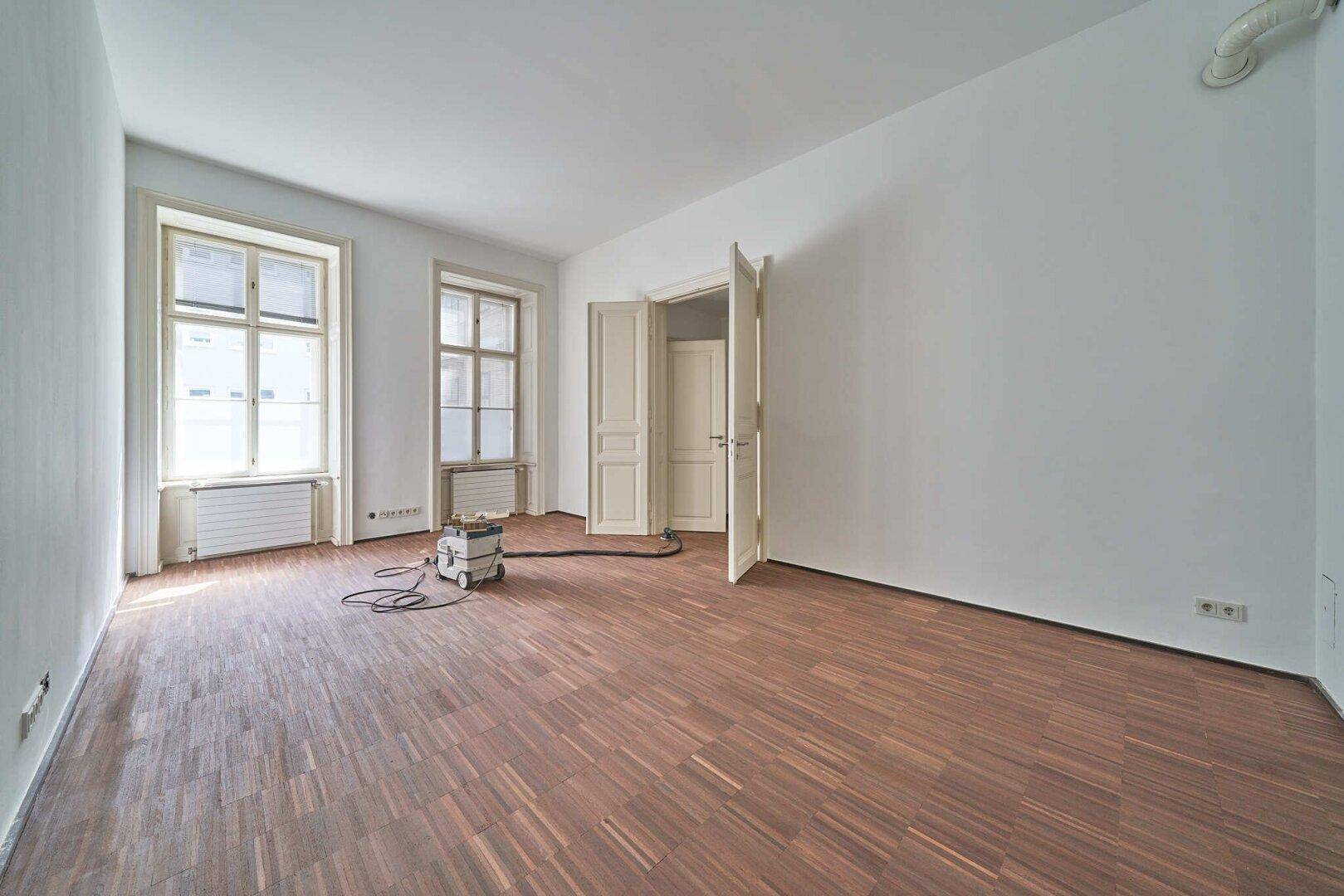 Leerer Raum mit Holzboden und zwei Fenstern, ideal für ein Schlafzimmer oder Büro.