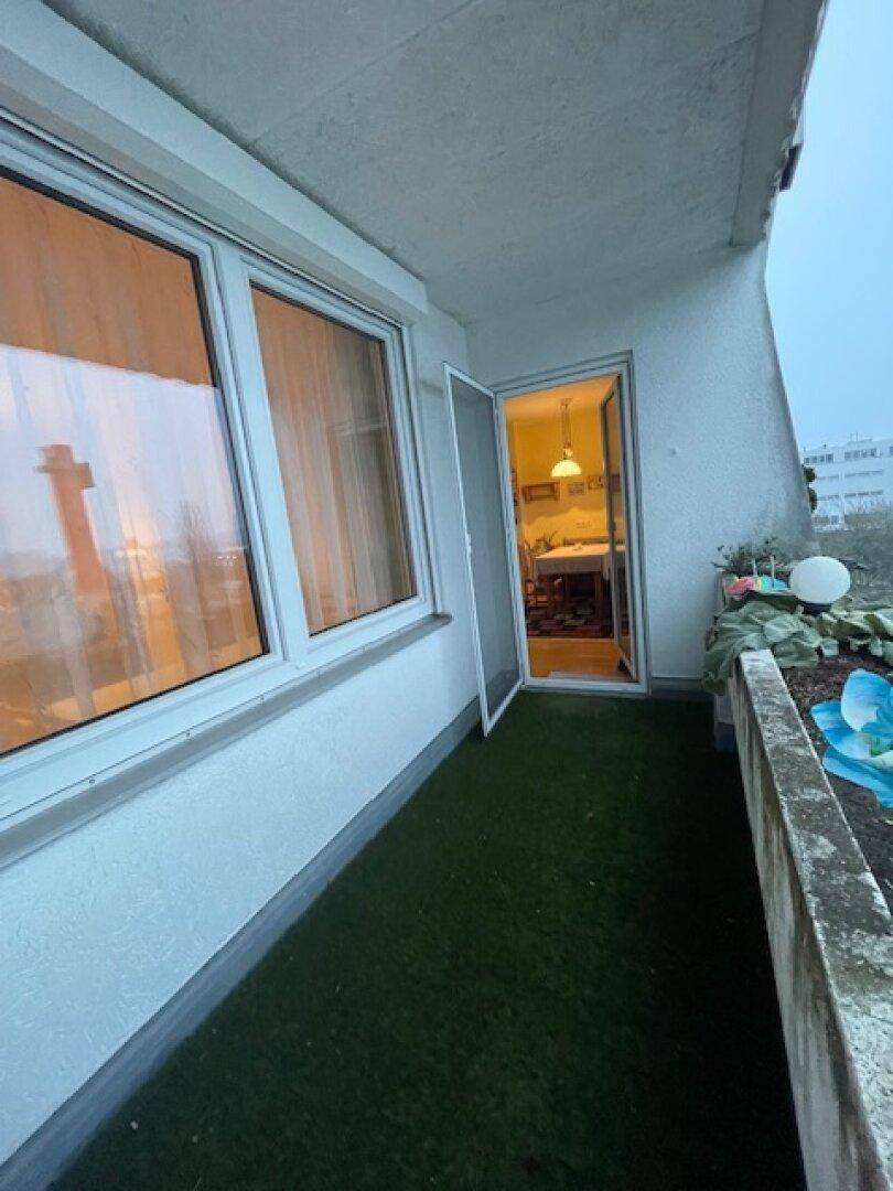 Schmaler Balkon mit Kunstrasen und Zugang zum Innenraum bei Dämmerung.