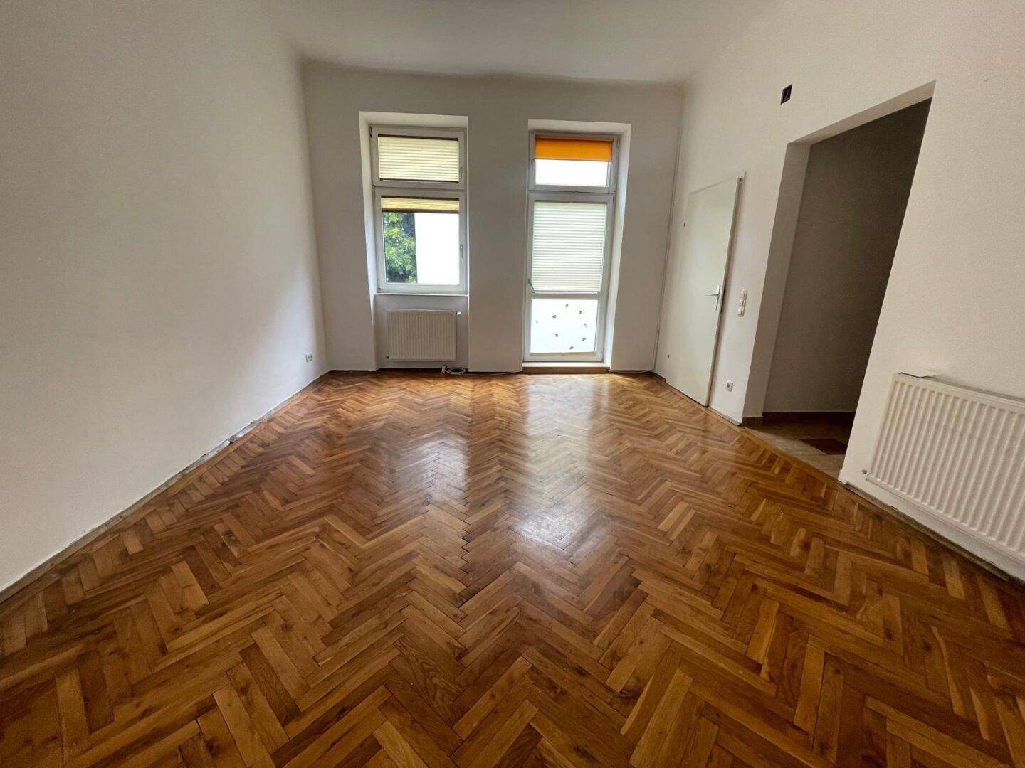Heller Raum mit schönem Fischgrätparkett und Blick nach draußen durch die Fenster.