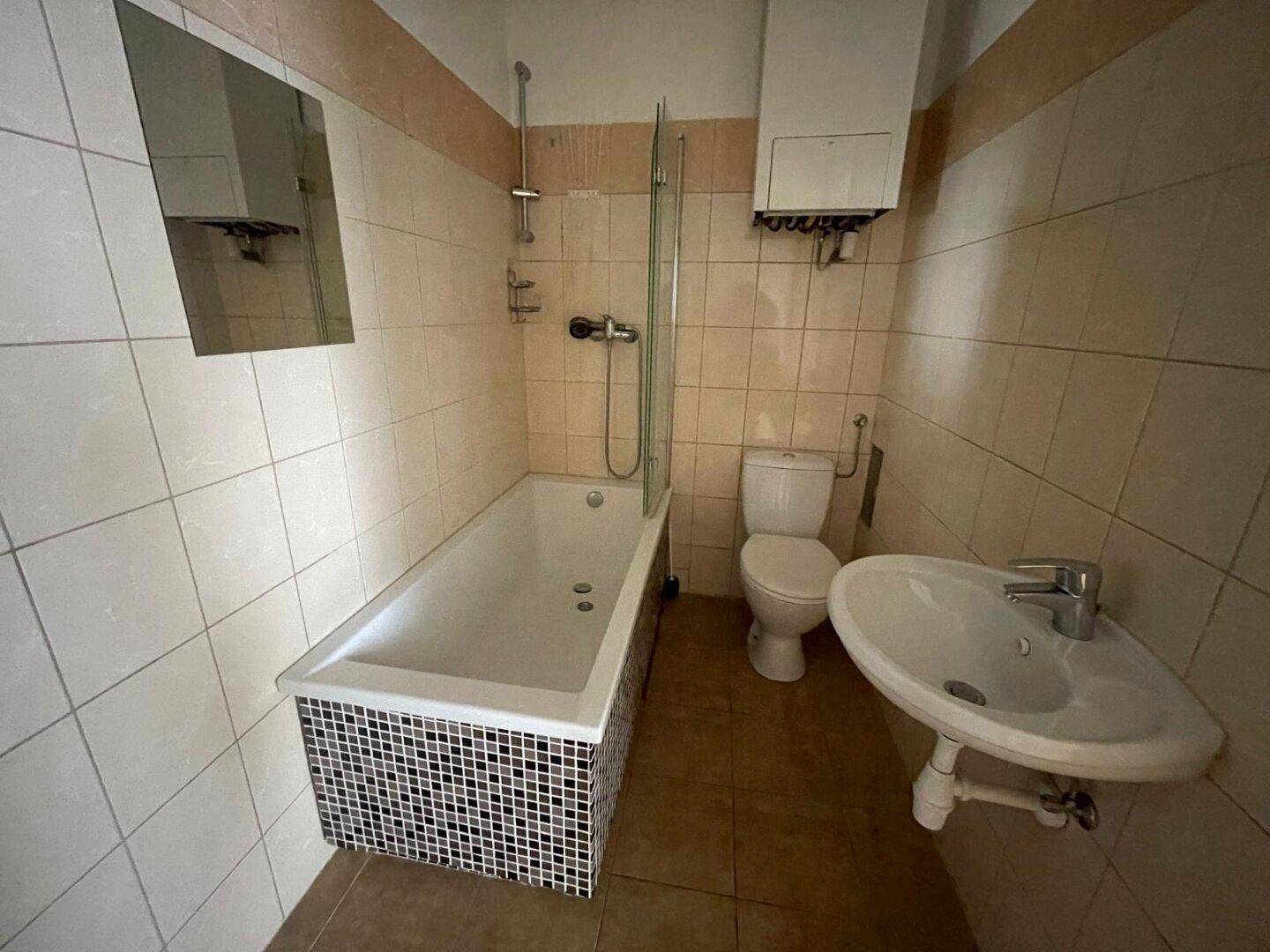 Badezimmer mit Badewanne, WC und Waschbecken, ausgestattet mit hellen Fliesen und einem Boiler.