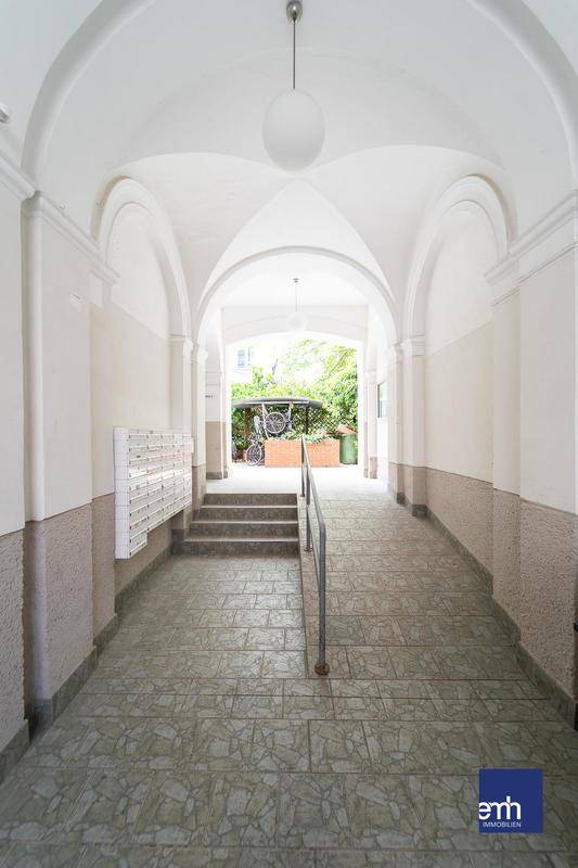 Gewölbter Eingangsbereich mit Fliesenboden, Briefkästen und Rampe zum Innenhof.
